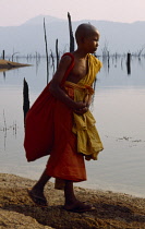 Religion, Buddhism, young monk wearing orange robes walking next to water.