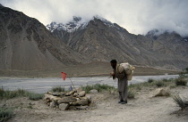 Pakistan, Korakorams, Porter carrying bundle on his back standing next to a shrine to dead porters.