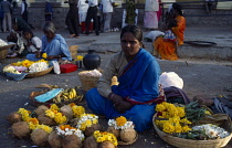 India, Karnataka, Mysore, Woman selling temple offerings of fruit and flowers seated on roadside.