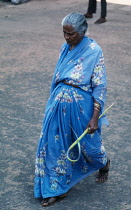India, Goa, Margao, Palm Sunday. Elderly woman dressed in blue sari with flower print carrying shaped palm frond.