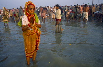 India, West Bengal, Sagar, Sagar Festival pilgrims elderly woman wearing red and yellow sari praying in water in foreground.
