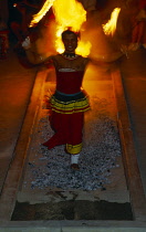 Sri Lanka, Kandy, Young man taking part in fire walking ceremony walking barefoot across hot coals carrying lighted flares.