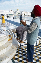 India, Punjab, Amritsar, Barefooted Sikh men praying at shrine in the Golden Temple complex with garland of marigold flowers laid across marble steps.