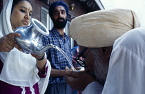India, Delhi , Woman pouring water for Sikh pilgrim to wash at temple.