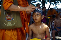 Thailand, Bangkok , Klong Toey , Wat Sapan. Novice ordination young boy having his head shaved by standing monk.