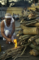 India, Calcutta, Hindu cremation. Son lighting his father s funeral pyre under partly covered body.