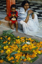 India, Uttar Pradesh, Varanasi , Woman with young child and temple offerings of marigold flowers.