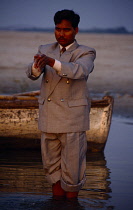 India, Uttar Pradesh, Varanasi , Man wearing suit with the trousers rolled up to stand in the River Ganges and pray.
