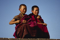 China, Qinghai Province, General, Two young Tibetan novice monks sitting on rooftop to watch festival celebrations.