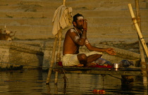 India, Uttar Pradesh, Varanasi, Saddhu praying on small platform raised above the River Ganges.