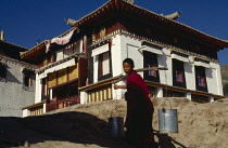 China, Qinghai, General, Young monk carrying water up to a temple in two buckets on a pole over his shoulder.