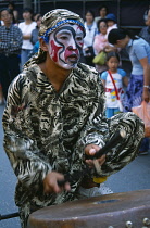 Thailand, North, Chiang Mai, Chinese New Year. Man wearing costume and face paints playing drums during procession.