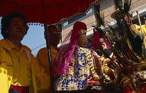 Thailand, North, Chiang Mai, Chinese New Year. Figures of Gods carried to temple in processional float with man and woman holding a red umbrella above them.