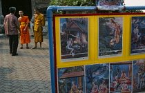 Thailand, North, Chiang Mai, Wat Bupparam Temple on Tha Phae Road. Display of artwork in the courtyard overlooked by two monks and visitor. Shows Hindu Buddhist links.