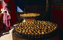 China, Tibet, Shigatse, Tashilhunpo Monastery. Large round trays of butter lamps burning with monk standing nearby.