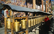 China, Tibet, Lhasa, Chagpo Ri. Painted carvings along a wall with monk spinning row of prayer wheels in front.