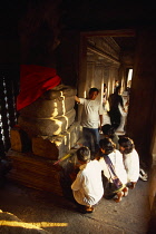 Cambodia, Siem Reap Province, Angkor Wat, Interior of shrine on the upper level with visitors lighting incense at base of Buddha figure seated below naga with multi headed hood.