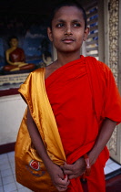 Sri lanka, Anuradhapura, Portrait of a young novice monk with a statue of Buddha in the background