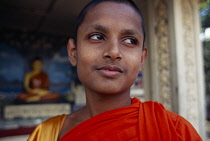 Sri lanka, Anuradhapura, Portrait of a young novice monk with a statue of Buddha in the background
