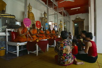 Thailand, Bangkok, Wat Pho. Small group of people sat in front of Monks praying. Monks sat in a row on white chairs holding up decorative signs.