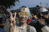 Thailand, Bangkok, Girl covered in mud  wearing goggles with fingers held in the peace sign  celebrating the Songkhran Festival. Thai New Year  15 April.