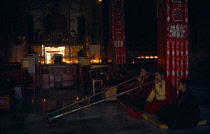 India, Bihar, Bodh Gaya, Karuna Tibetan Buddhist temple interior with monks kneeling on ground to blow long horns.