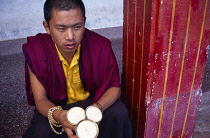 India, Sikkim, Rumtek, Young Buddhist monk wearing prayer beads wrapped around wrist and purple and yellow robes holding unlit yak butter candles.