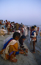 India, Uttar Pradesh, Allahabad, Magh Mela Festival,  Crowds gathered on shores of the River Ganges,  Woman and child in foreground lighting incense.