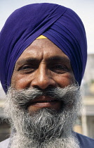 India, Delhi, Head and shoulders portrait of Sikh man with thick greying beard and moustache wearing purple turban.