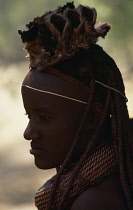 Namibia, People, Himba, Head and shoulders portrait of young Himba girl wearing traditional head dress and bead jewellery.