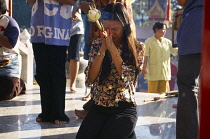 Thailand, Phuket, Wat Chalong, Girl kneeling to pray holding lotus flower and incense offerings.