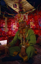 Thailand, Chiang Mai, Novice monk at ordination ceremony at Wat Chiang Yuen, Sitting cross-legged wearing ornate head dress and robes.