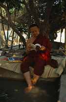 Thailand, North, Chiang Mai, Monk sitting under a tree reading a book trying to keep cool.