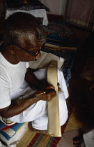 Sri Lanka, Matale, Looking down on man writing sutra on ola palm leaf.