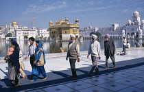 India, Punjab, Amritsar, Golden Temple also known as the Hari Mandir, Local people walking by the pool in the foreground with Temple undergoing renovations behind.