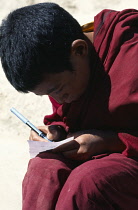 India, Ladakh, Tikse, Close up of a novice monk writing with a pen and paper at Tikse Monastery.