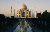 India, Uttar Pradesh, Agra, Taj Mahal in evening light reflected in rippled surface of watercourse through formal gardens in foreground with visitors on each side.