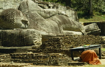 Sri Lanka, Polonnaruwa, Buddhist monk praying in front of giant reclining Buddha figure.