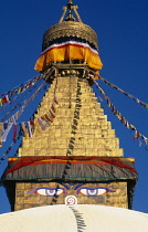 Nepal, Kathmandu, Bodhnath Stupa, Detail of gilded spire hung with prayer flags and with painted eyes at its base.