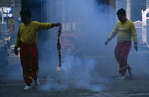 Thailand, North, Chiang Mai, Chinese New Year. Man holding chain of fire crackers ignited at one end partly obscured by smoke.