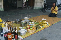 Thailand, North, Chiang Mai, Chinese New Year, Shopkeepers offerings of food and drink laid out on matting with lighted incense sticks, Female worshipper kneeling at end.
