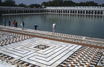 India, Delhi, Pilgrims on decorated edge of temple pool.