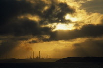 Wales, Pembrokeshire, Milford Haven, Distant view over sea towards Texaco oil refinery in golden light with low grey cloud.