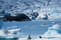 Iceland, Jokulsarlon Island, Distant boat on glacial lagoon with icebergs and glacial landscape.