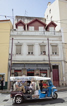 Portugal, Estremadura, Lisbon, Alfama district, Tuk Tuk full of tourist passing cafe.