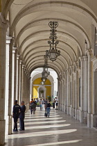 Portugal, Estremadura, Lisbon, Baixa, Praca do Comercio, Tourists walking along colonnade next to Rua Augusta triumphal arch.