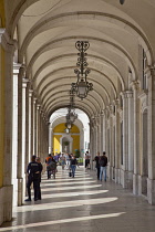 Portugal, Estremadura, Lisbon, Baixa, Praca do Comercio, Tourists walking along colonnade next to Rua Augusta triumphal arch.
