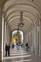 Portugal, Estremadura, Lisbon, Baixa, Praca do Comercio, Tourists walking along colonnade next to Rua Augusta triumphal arch.