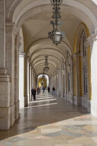 Portugal, Estremadura, Lisbon, Baixa, Praca do Comercio, Tourists walking along colonnade next to Rua Augusta triumphal arch.