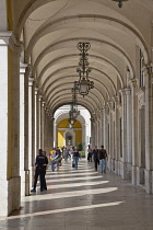 Portugal, Estremadura, Lisbon, Baixa, Praca do Comercio, Tourists walking along colonnade next to Rua Augusta triumphal arch.